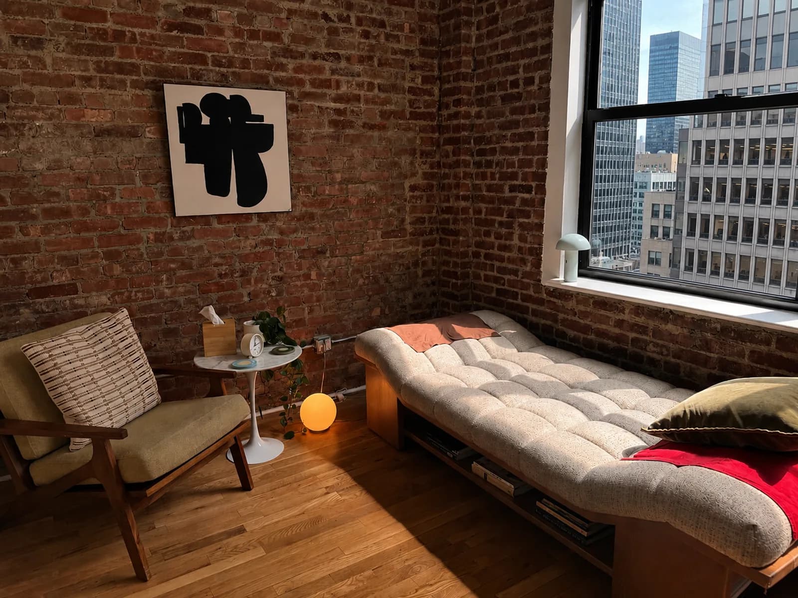 A therapy room at Gotham Group Practice: exposed brick, a daybed under a tall window, and a reading chair